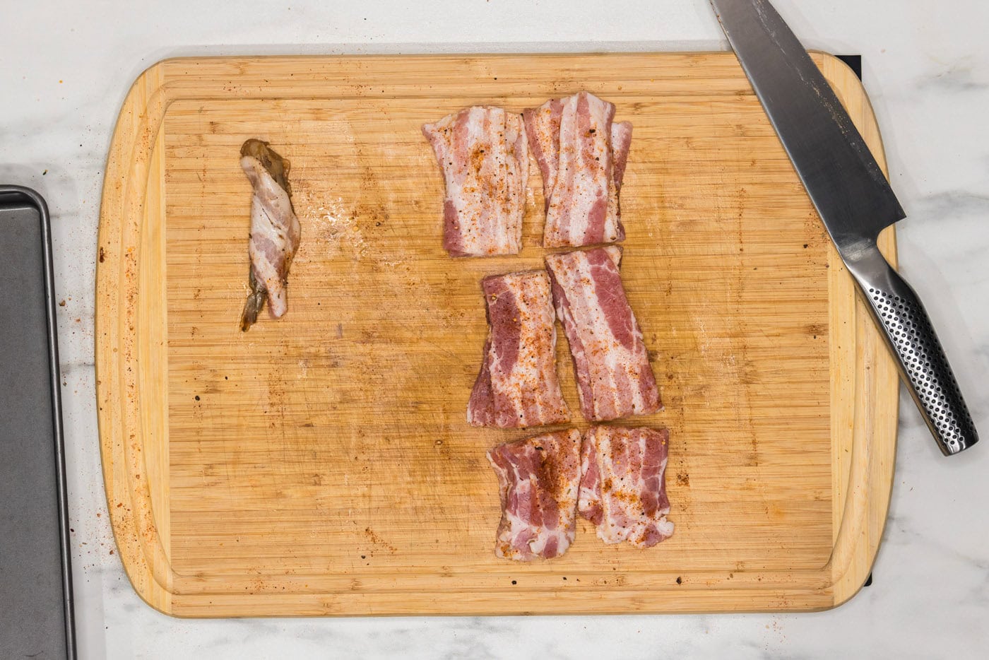 bacon wrapped shrimp next to bacon slices on a cutting board