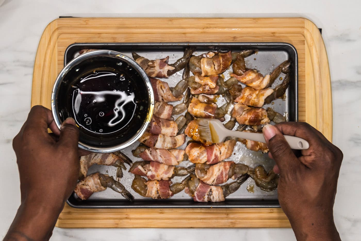 pouring soy sauce mixture over bacon wrapped shrimp on a baking sheet