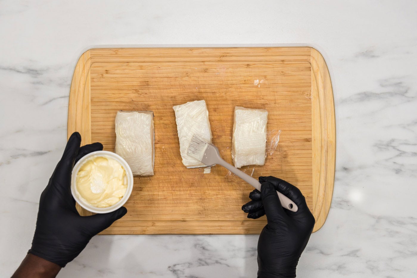 brushing Chilean sea bass with softened butter on a cutting board