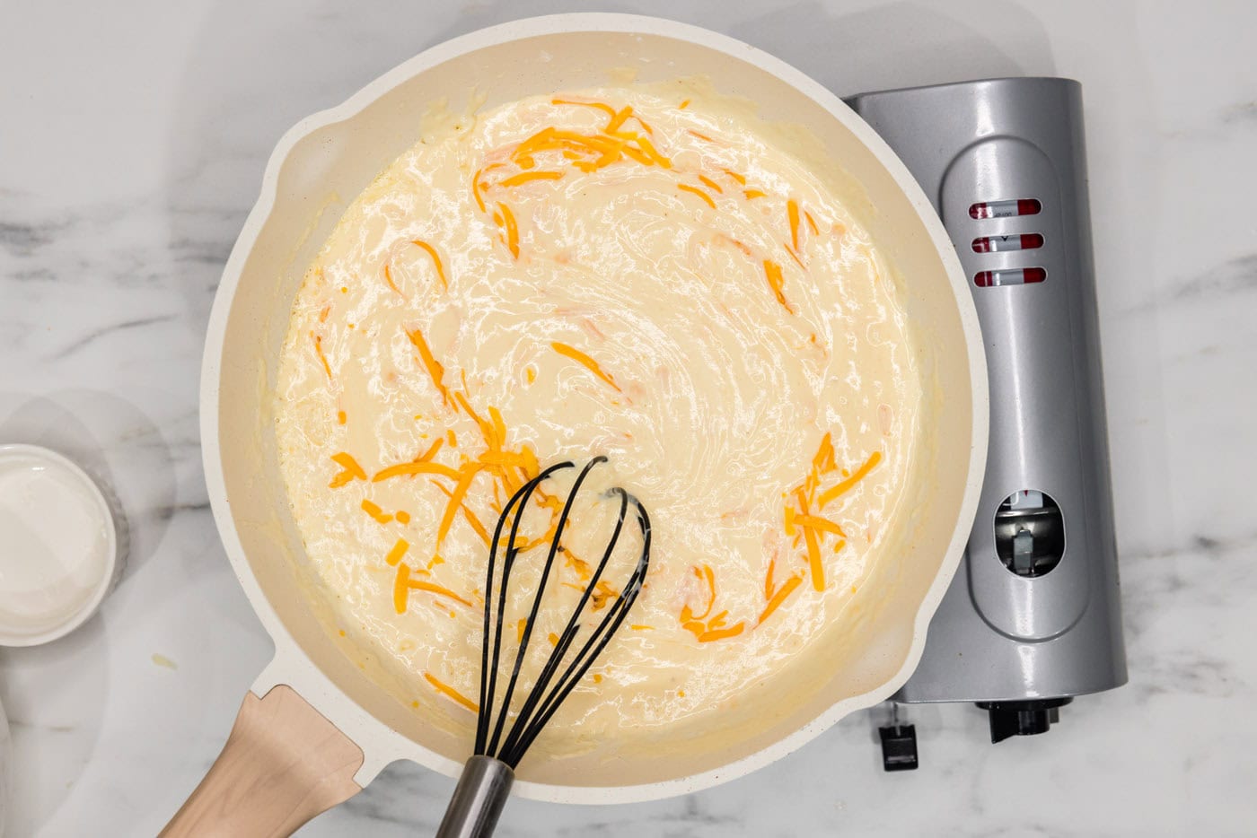 whisking shredded cheese into béchamel in a skillet