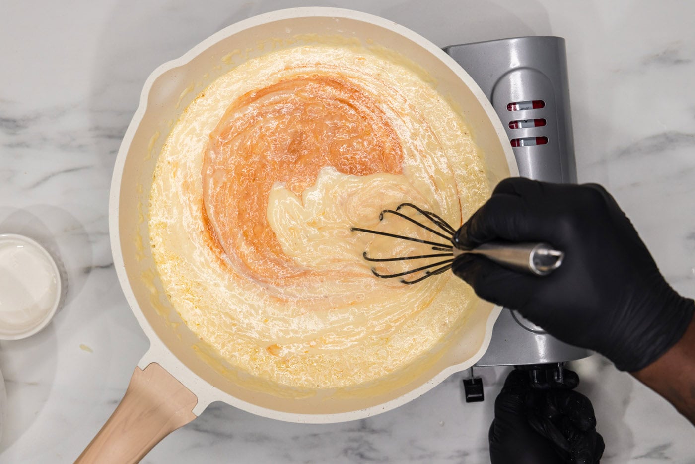 whisking hot sauce into mac and cheese sauce in a skillet