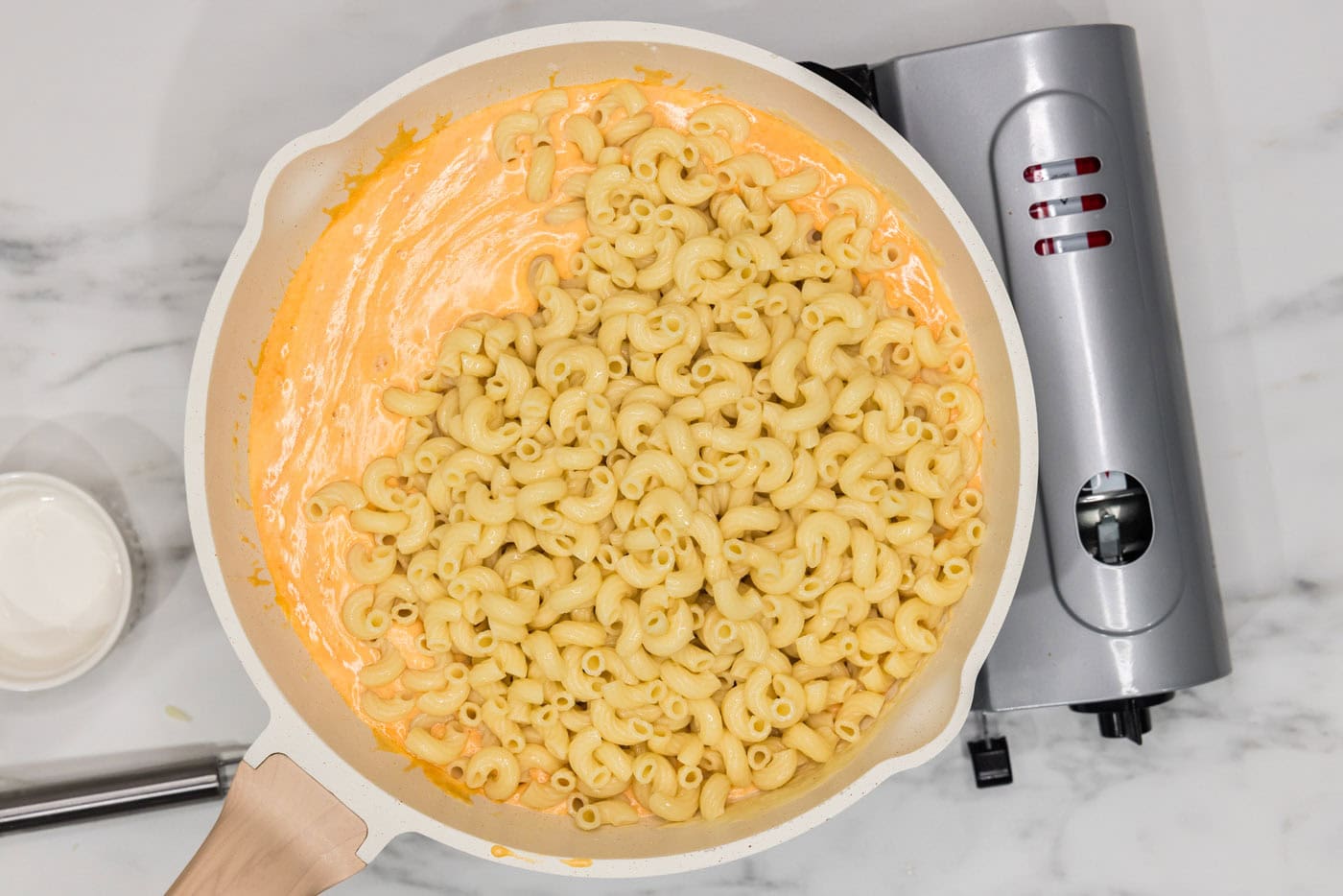 elbow macaroni noodles added to buffalo cheese sauce in a skillet