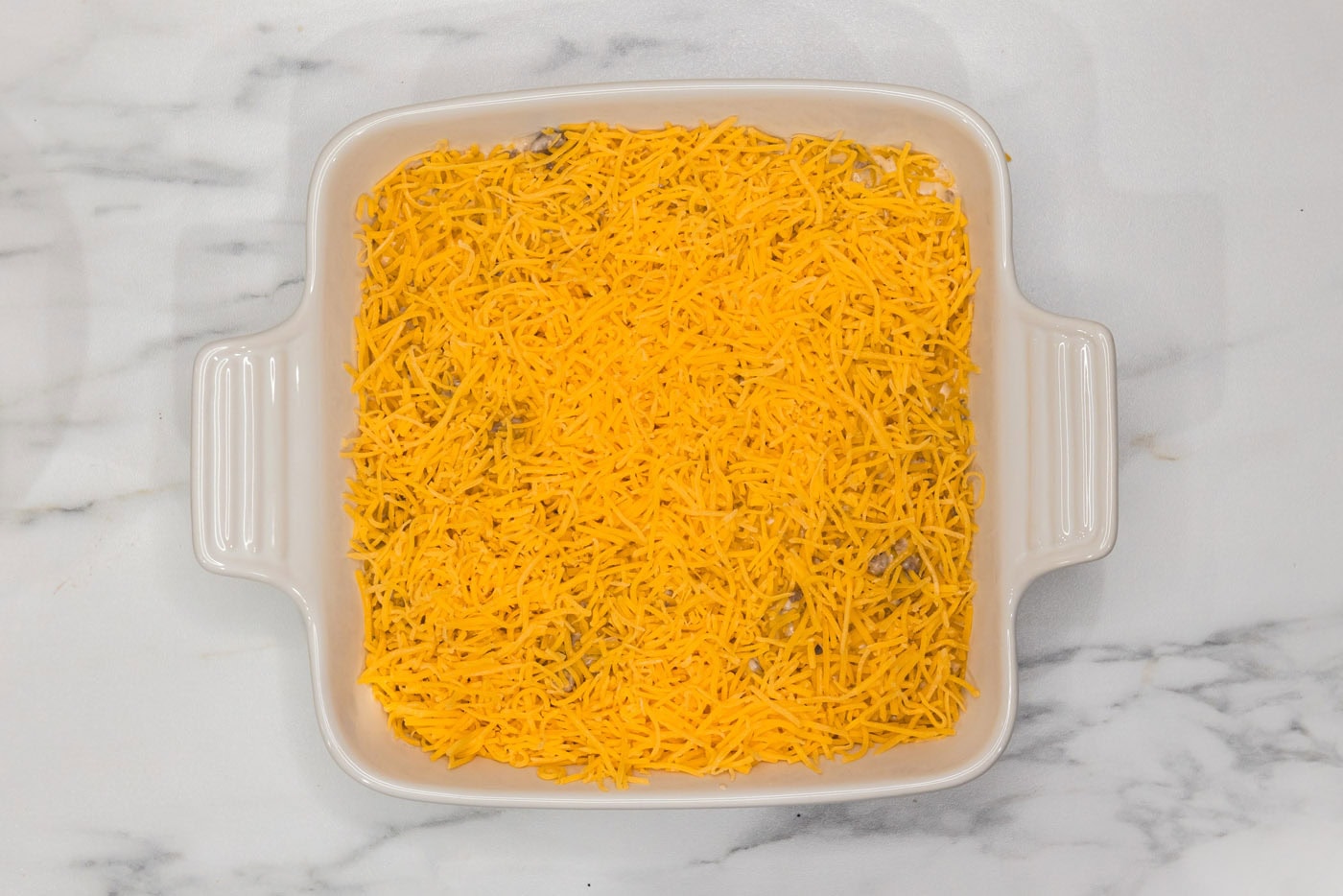 shredded cheddar cheese on top of cheeseburger dip in a dish