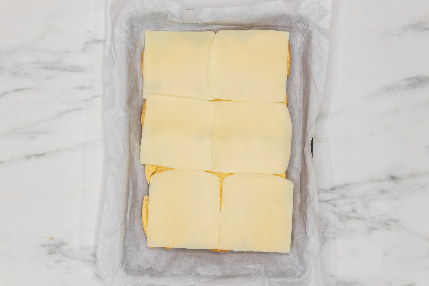 sliced mozzarella on top of slider buns in a baking dish