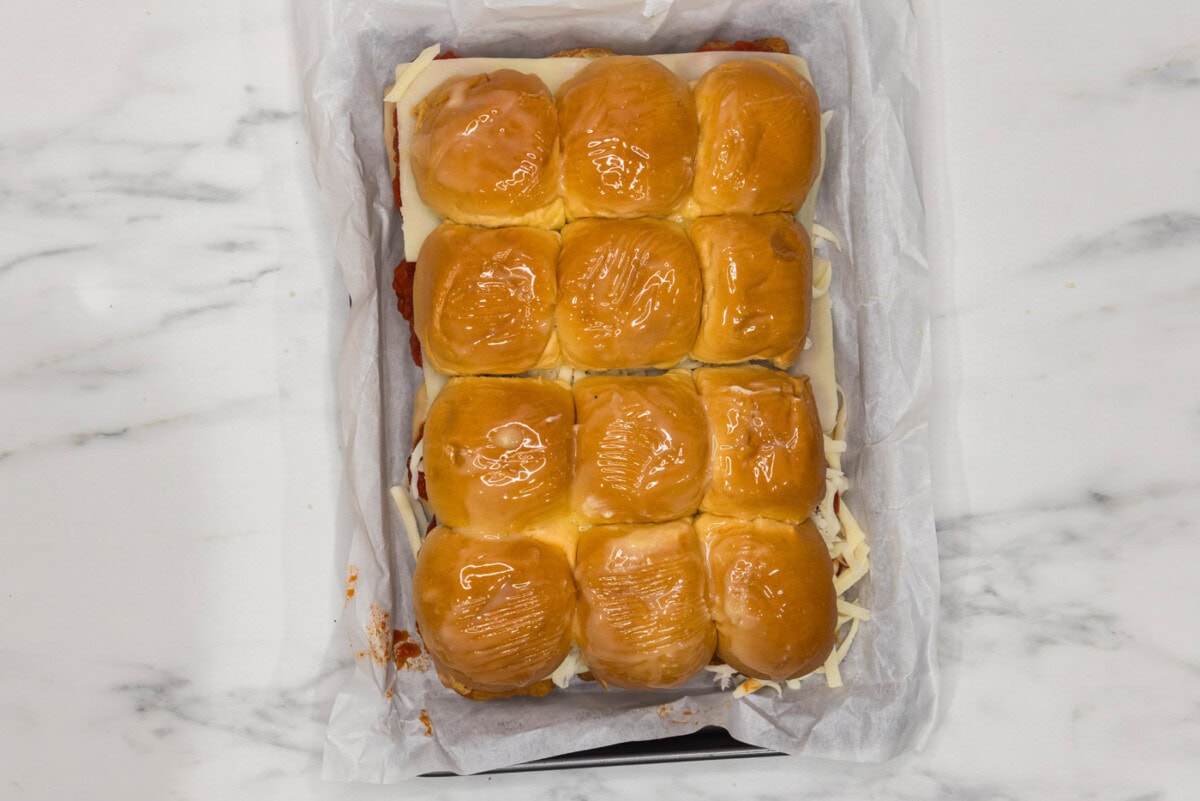 chicken parmesan sliders topped with melted butter in a baking dish