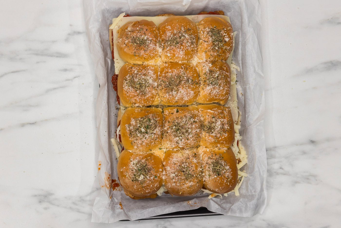 chicken parmesan sliders in a baking dish with parmesan cheese and italian seasoning