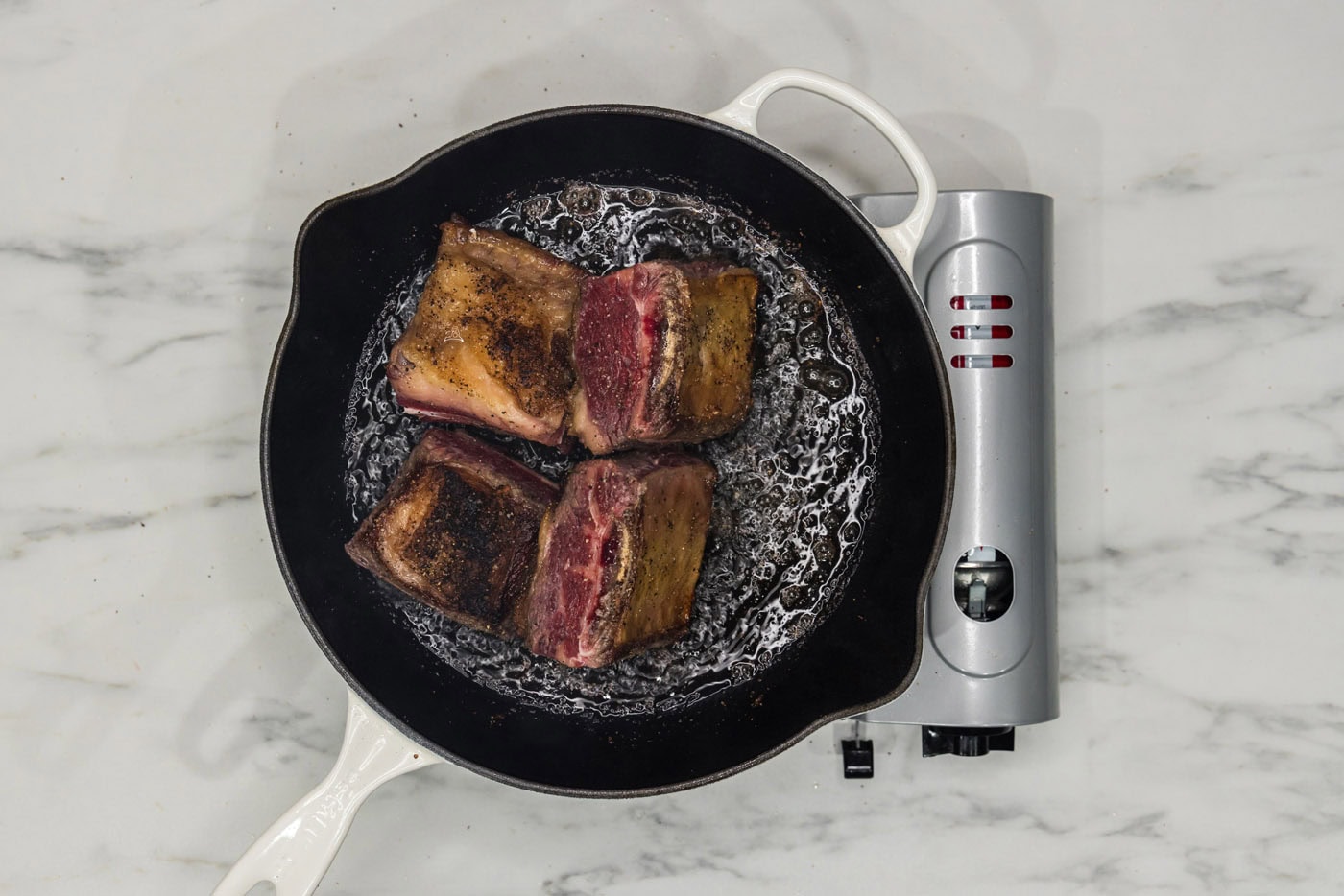 beef short ribs searing in a skillet of oil