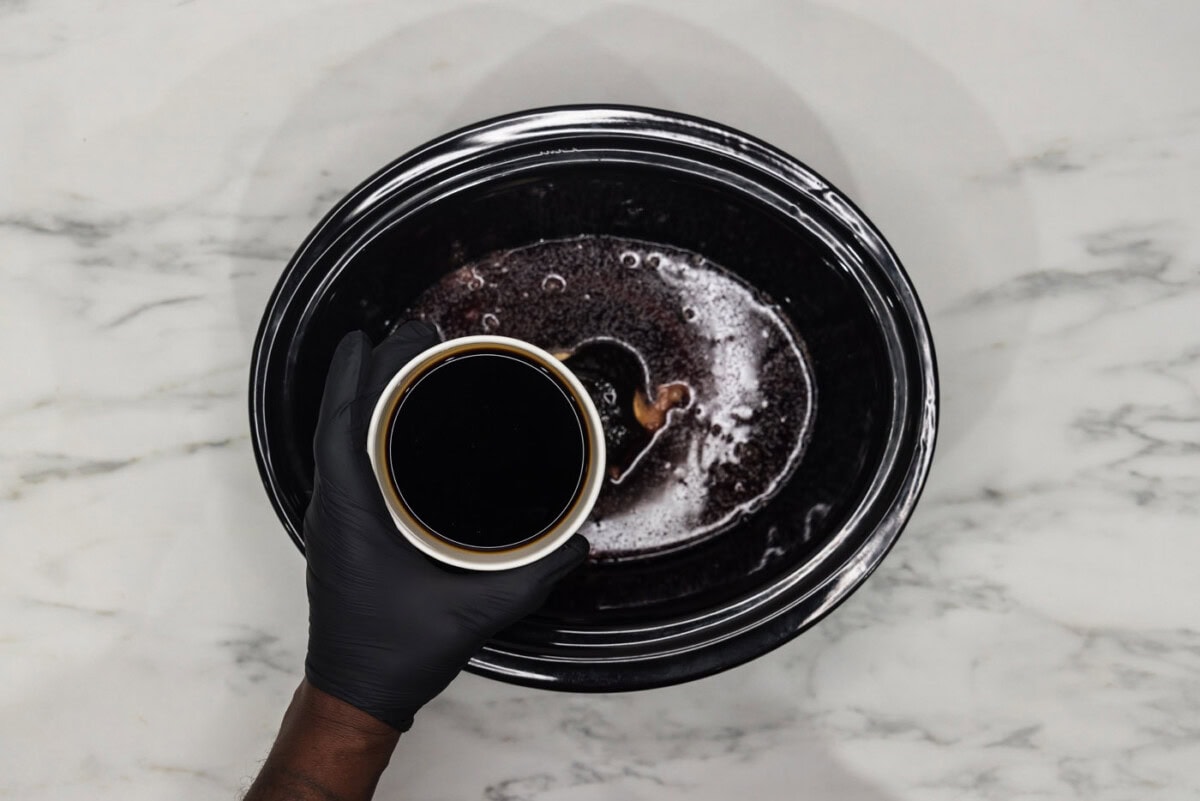 pouring red wine into crockpot with seasonings and soy sauce
