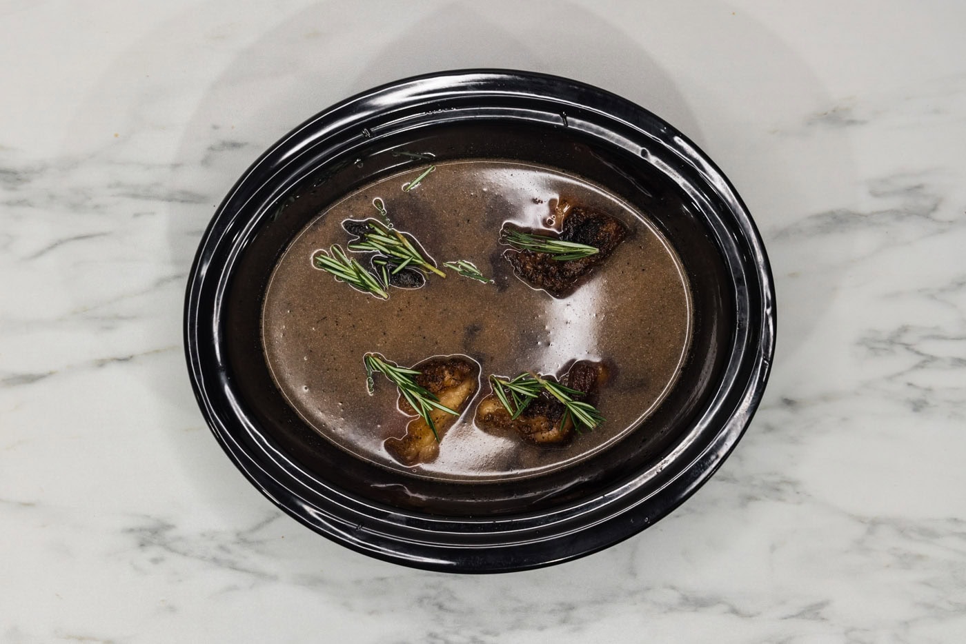 rosemary sprigs on top of crockpot beef short ribs