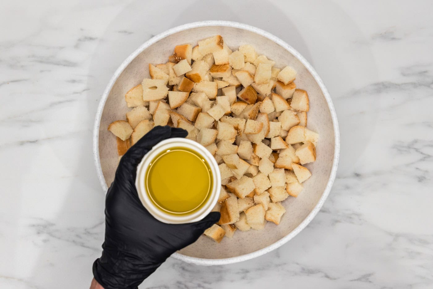 olive oil held over a bowl of cubed bread