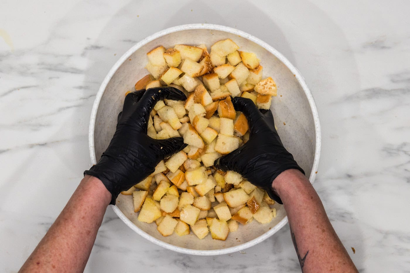 gloved hands mixing croutons with olive oil