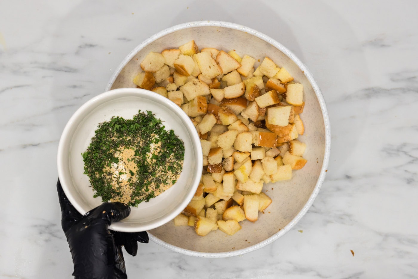 bowl of seasonings and herbs held over a bowl of cubed bread