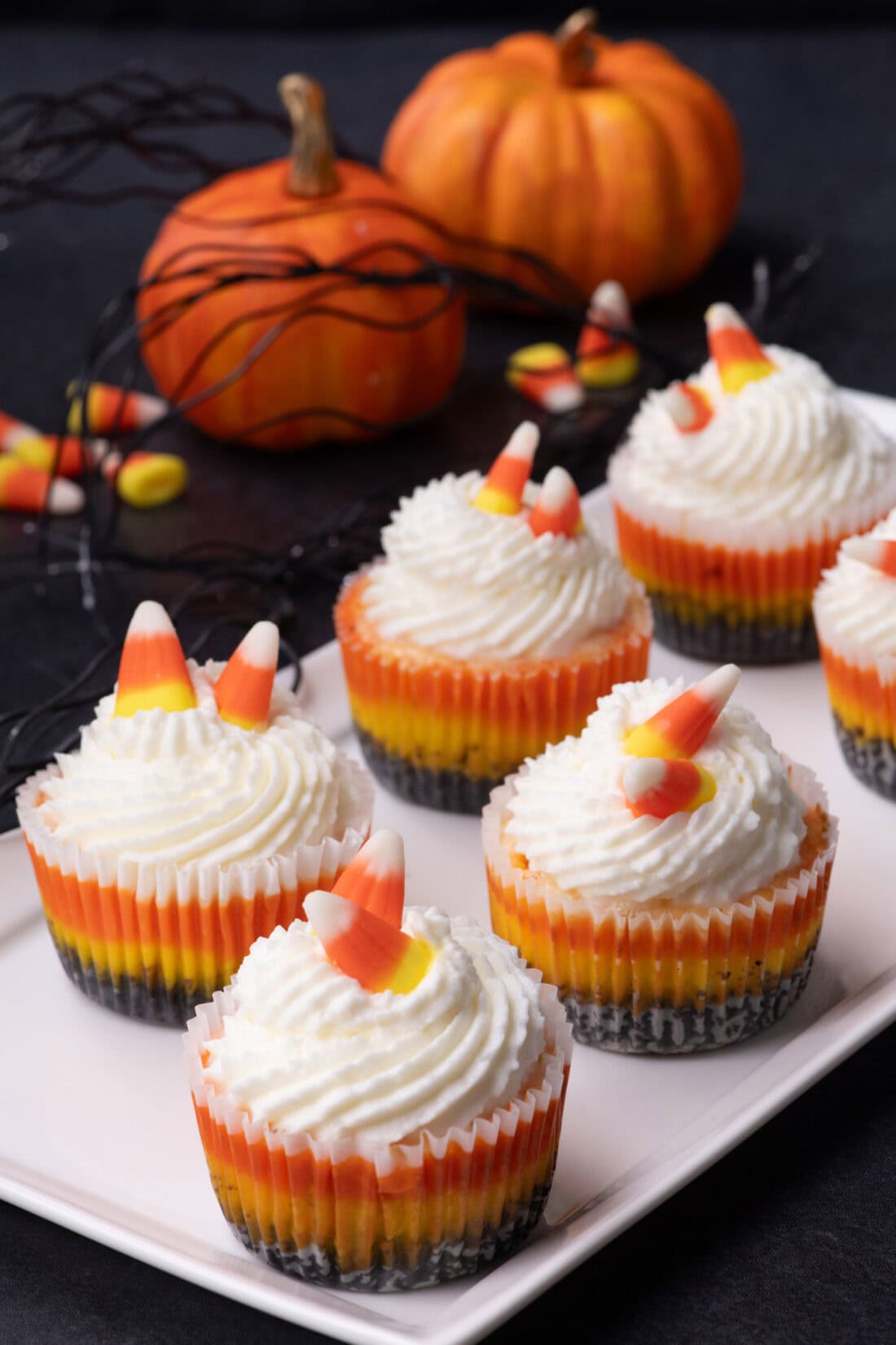 Mini Candy Corn Cheesecakes on a white platter with pumpkins in the background