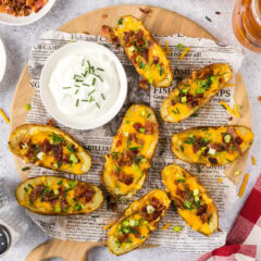 Potato Skins on a parchment lined wooden platter with a bowl of sour cream