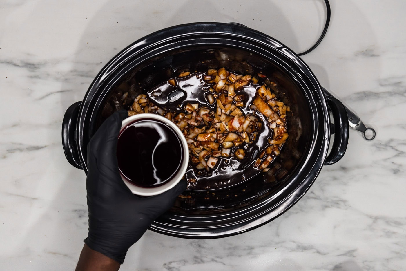 adding red wine to crockpot with onion, tomato paste, soy sauce, and beef base