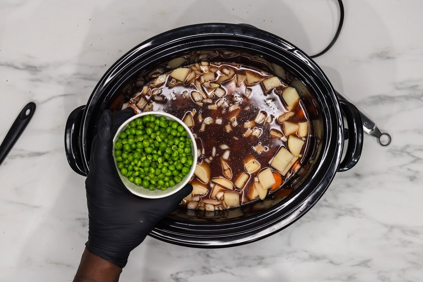 adding peas to potato and oxtail stew in crockpot