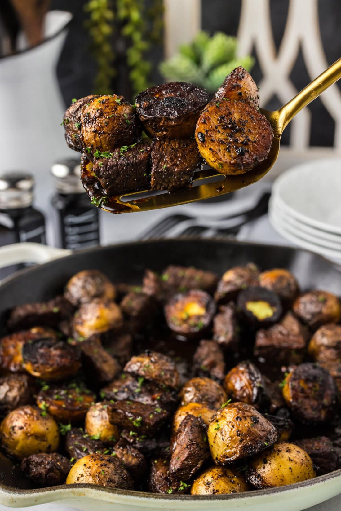 Spatula of Steak and Potatoes held above a skillet full of Steak and Potatoes