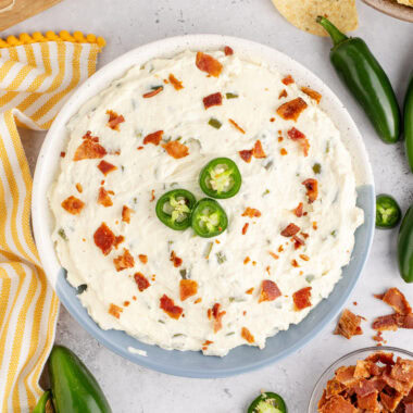 Close up photo of a bowl of Crockpot Jalapeno Popper Dip topped with bacon and jalapeno slices