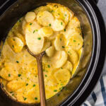 Close up photo of a spoon in a Crockpot full of scalloped potatoes