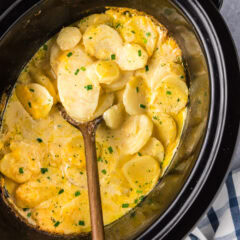 Close up photo of a spoon in a Crockpot full of scalloped potatoes