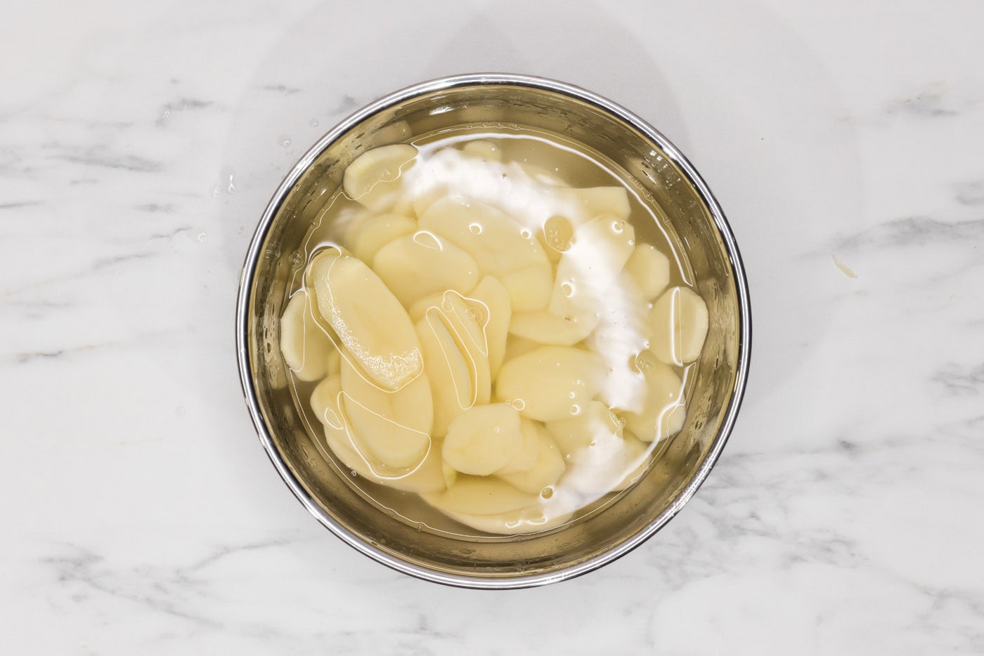 thinly sliced potatoes in a bowl of water