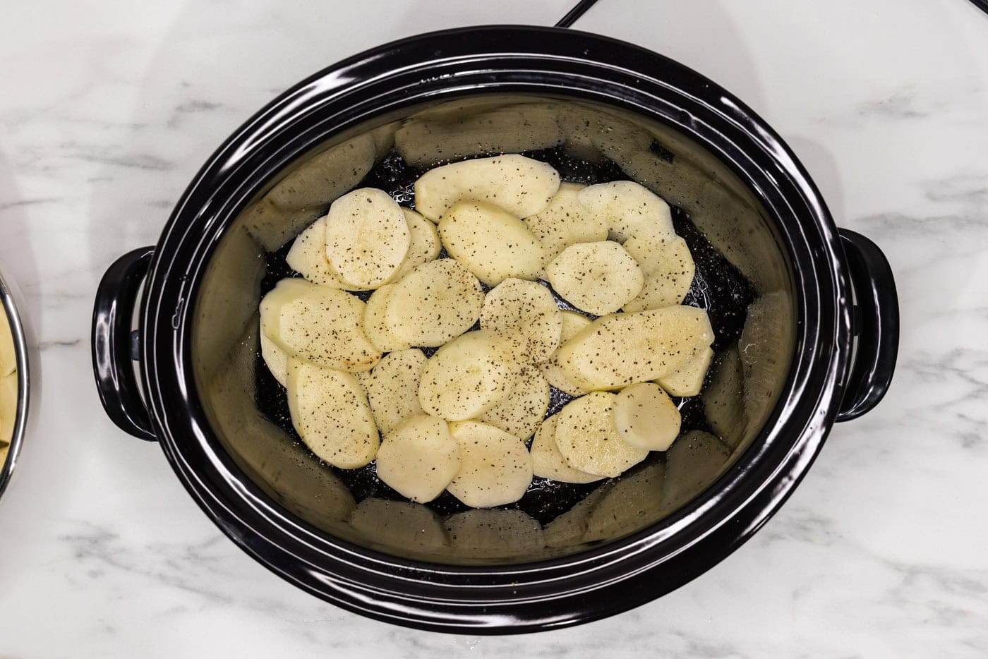 seasoned and sliced potatoes in a crock of a slow cooker