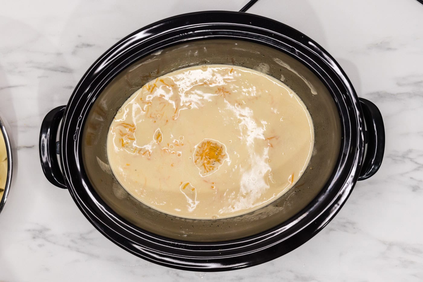 cheese sauce on top of sliced potatoes in a crockpot