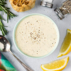 Close up photo of a bowl of Garlic Aioli with lemons, garlic and seasonings around it