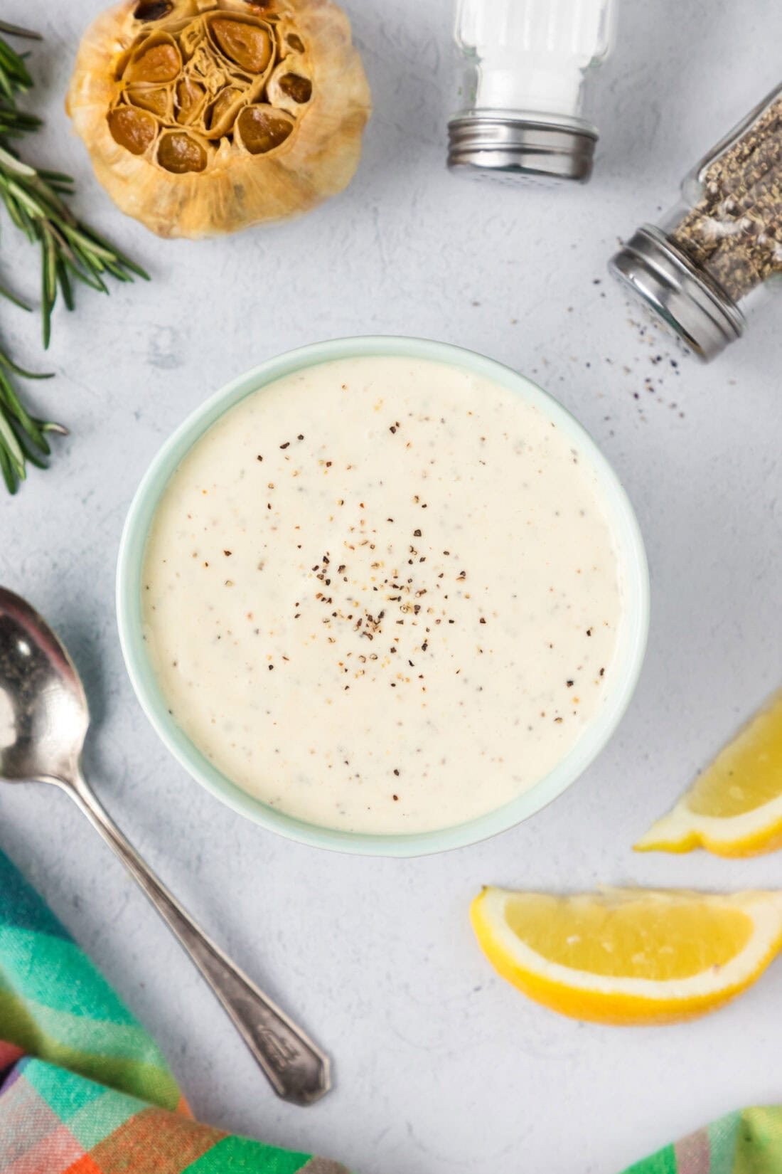 Bowl of Garlic Aioli with salt, pepper lemons and garlic to the side