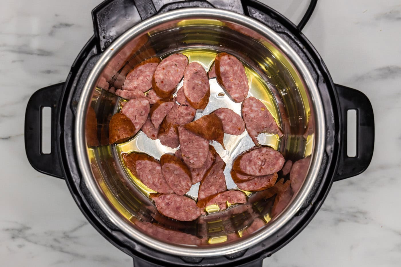 andouille sausage cooking with olive oil in a pressure cooker