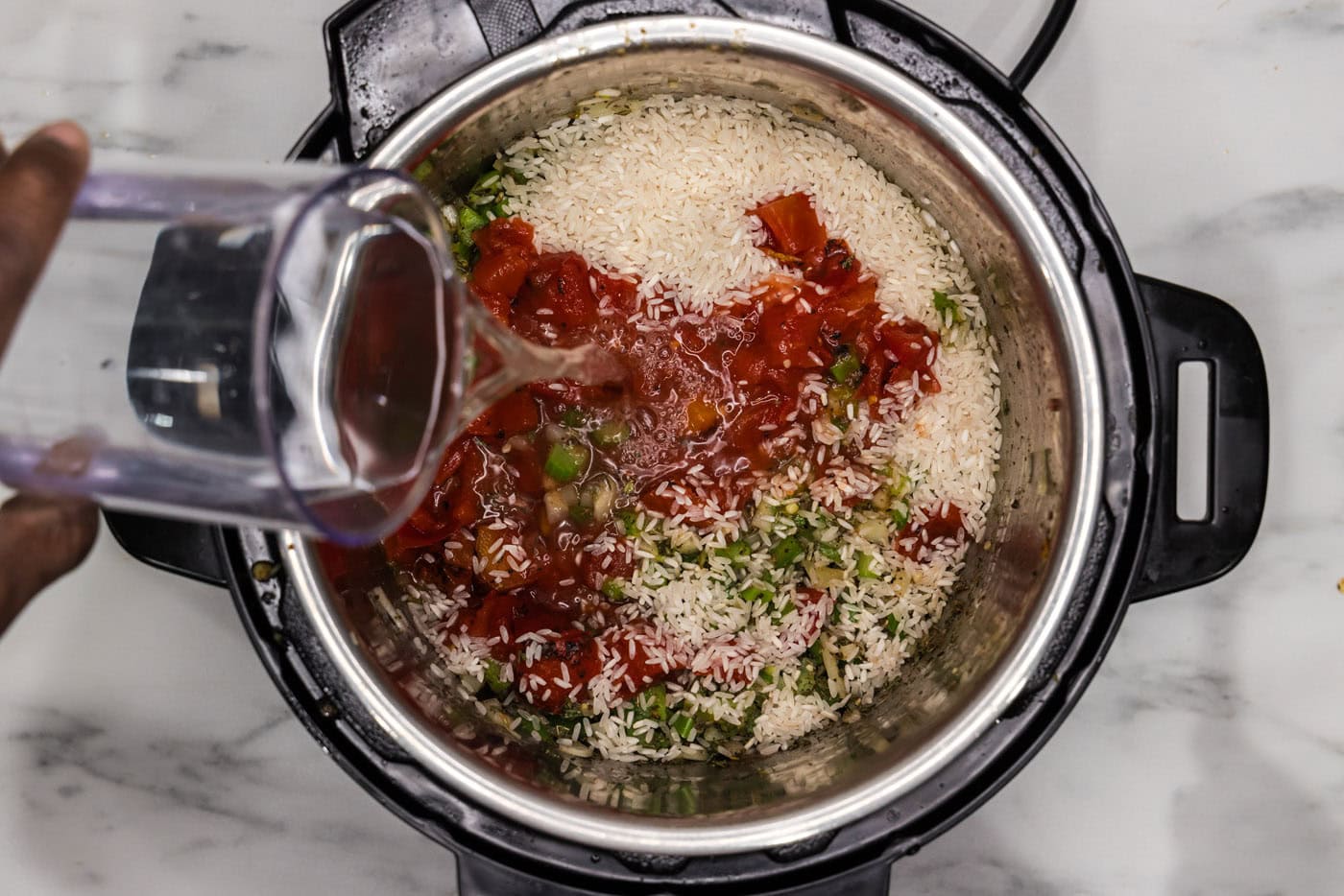 pouring water into instant pot with jambalaya ingredients