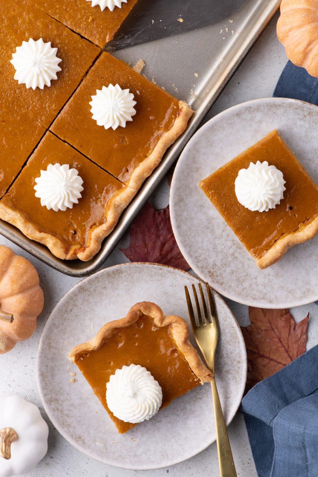 Two pieces of Pumpkin Slab Pie on plates topped with whipped cream