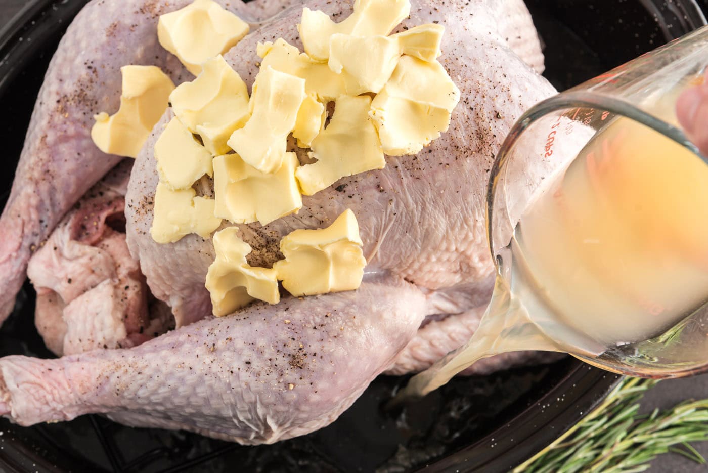 pouring chicken broth into roasting pan with turkey