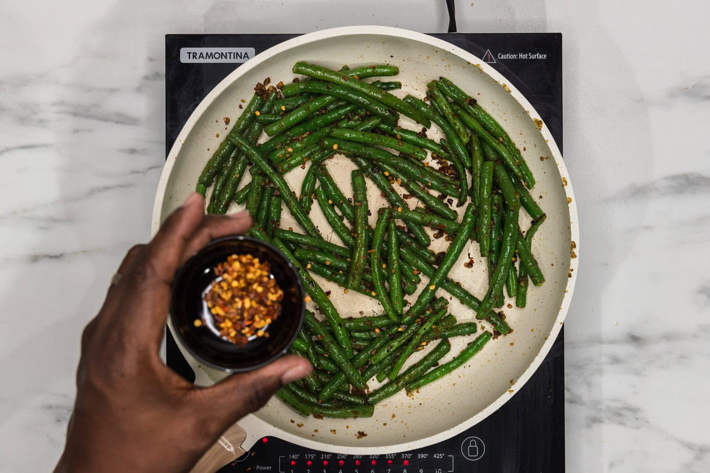 hand holding red pepper flakes over sauteed green beans