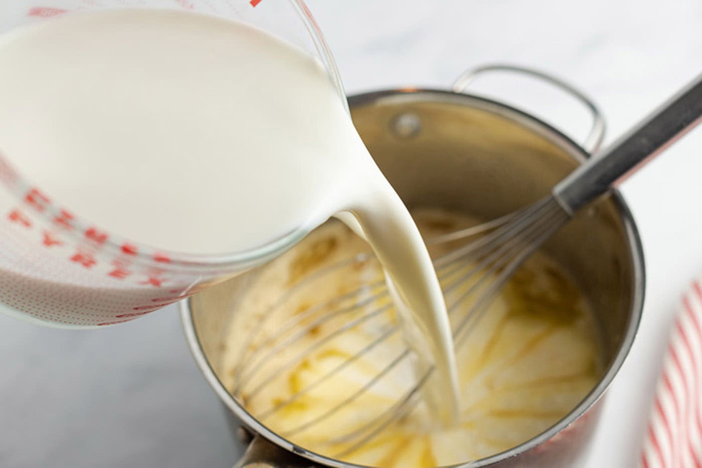 Milk being added to the egg mixture in a saucepan