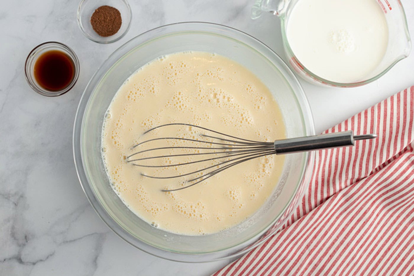 Egg mixture in a bowl with vanilla, nutmeg and milk to the side