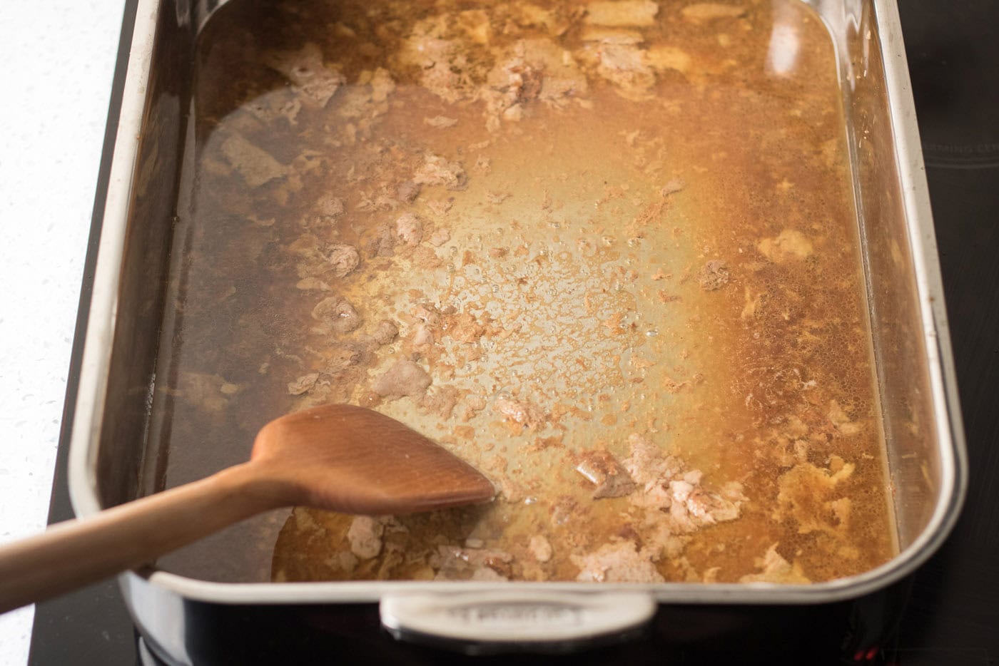 Spatula in a roasting pan full of pan drippings