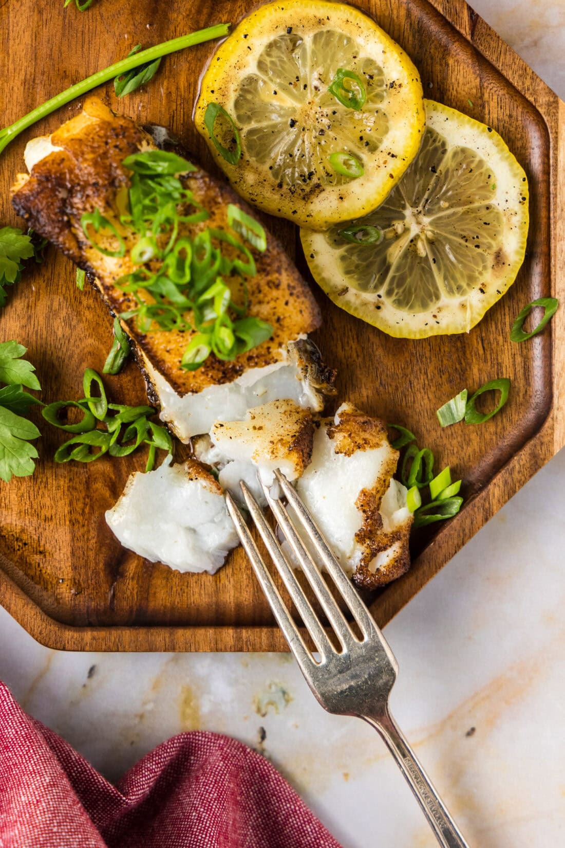 Overhead photo of a Pan Seared Chilean Sea Bass filet on a plate with a fork and lemons on the side