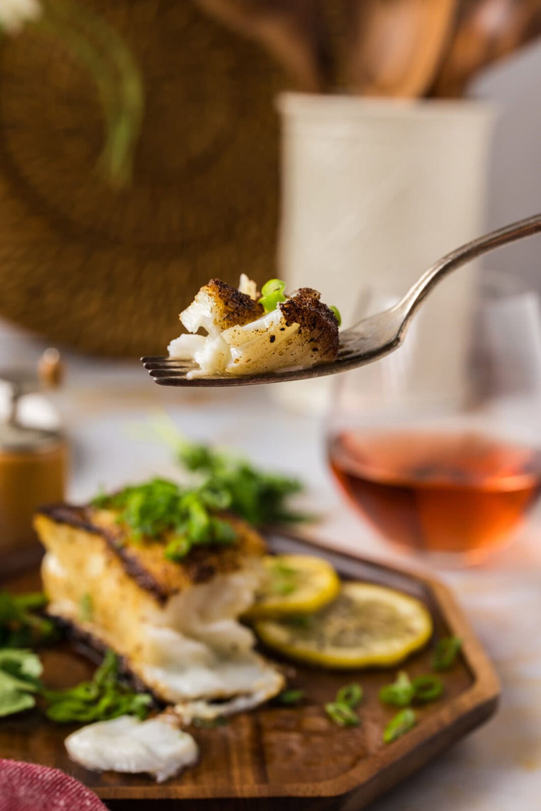 Piece of Pan Seared Chilean Sea Bass on a fork held above a plate of Pan Seared Chilean Sea Bass