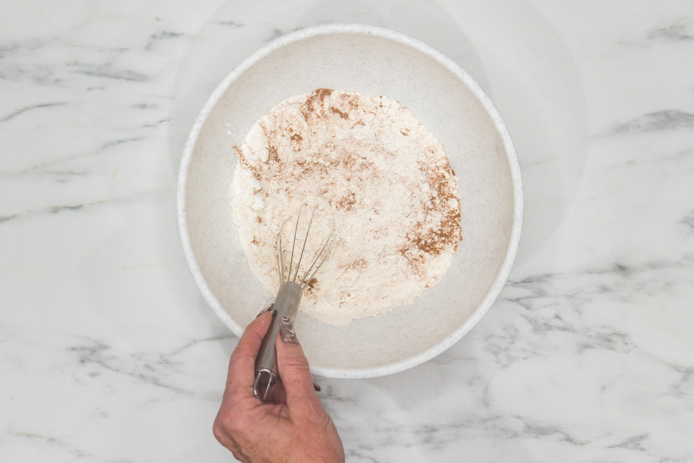 hand whisking flour, cinnamon, baking soda, and baking powder in a bowl