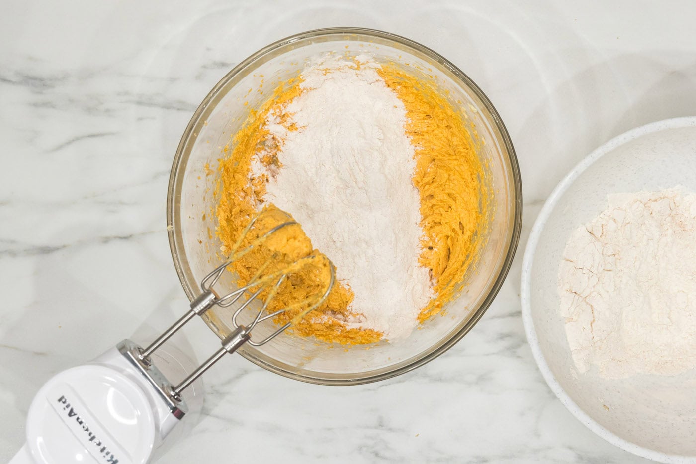 adding dry ingredients to wet ingredients in a bowl with a hand mixer