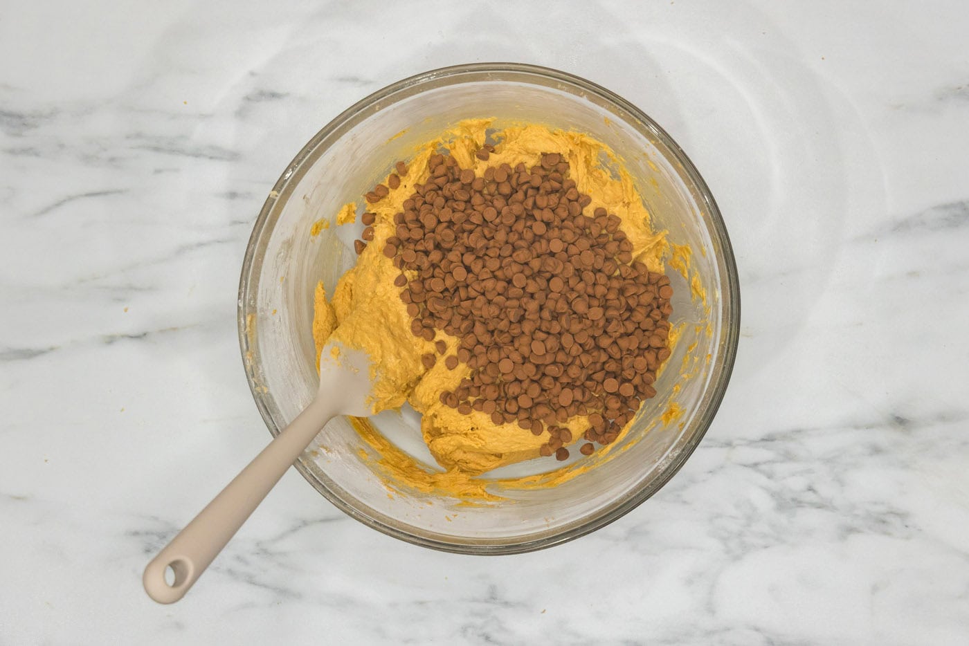 adding cinnamon chips to a bowl of pumpkin cookie dough