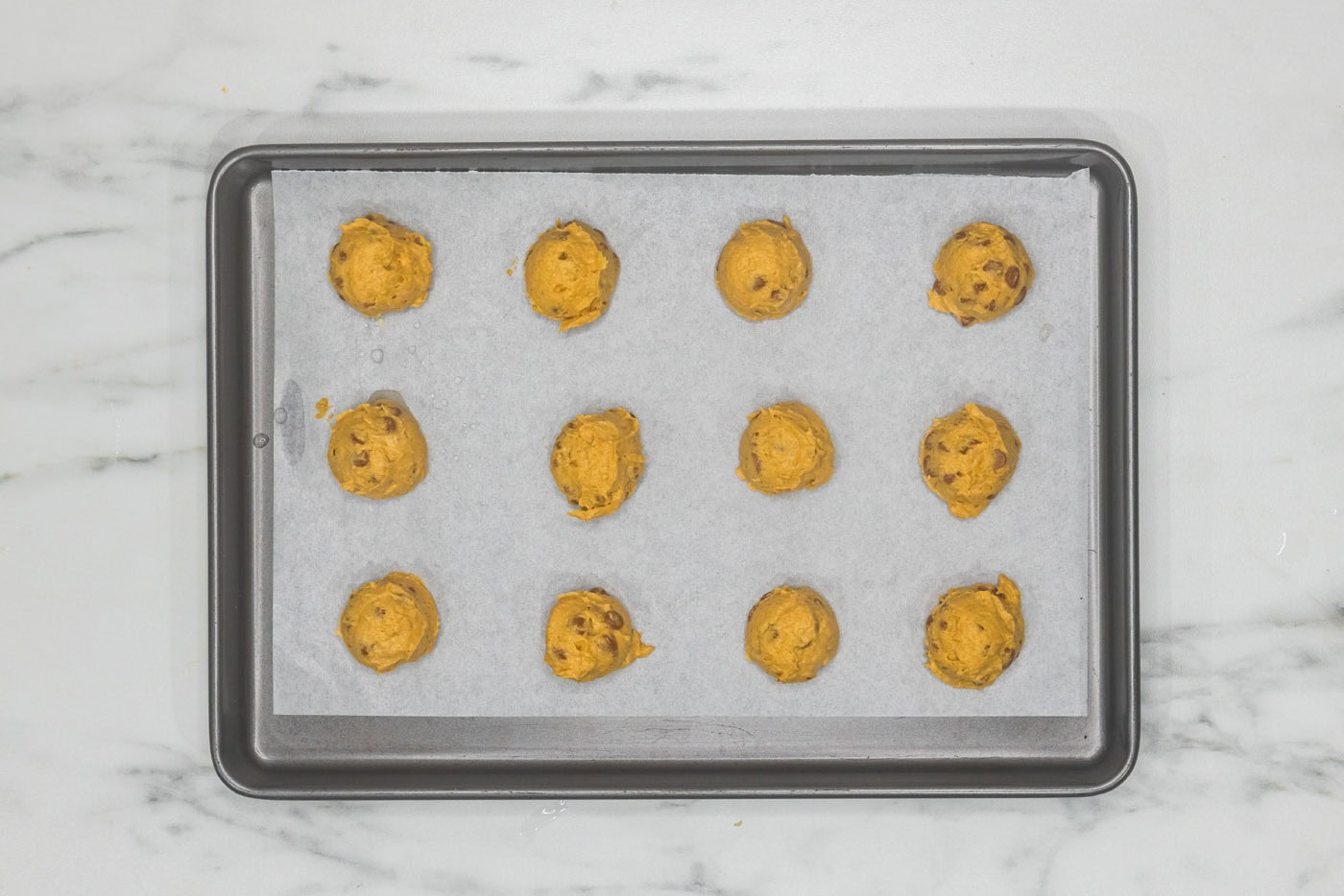 pumpkin cinnamon chip cookie dough balls on a lined baking sheet