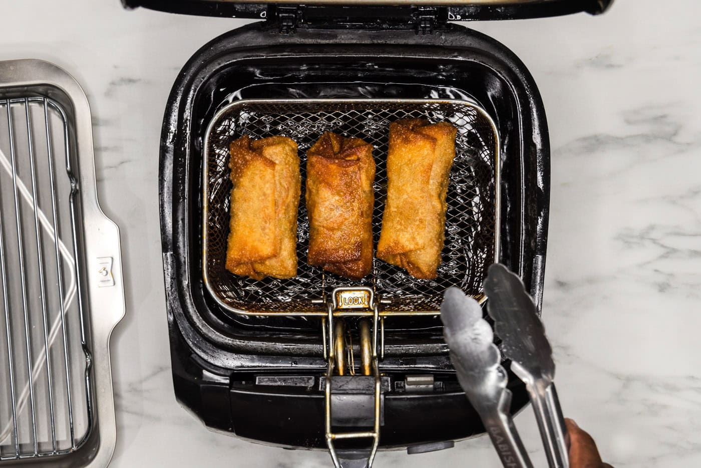 tongs grabbing deep fried egg roll from basket