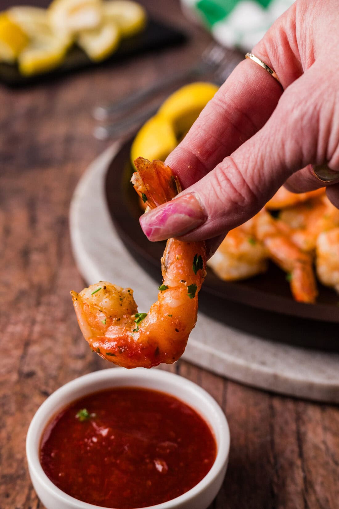 Hand holding a Steamed Shrimp above a bowl of cocktail sauce