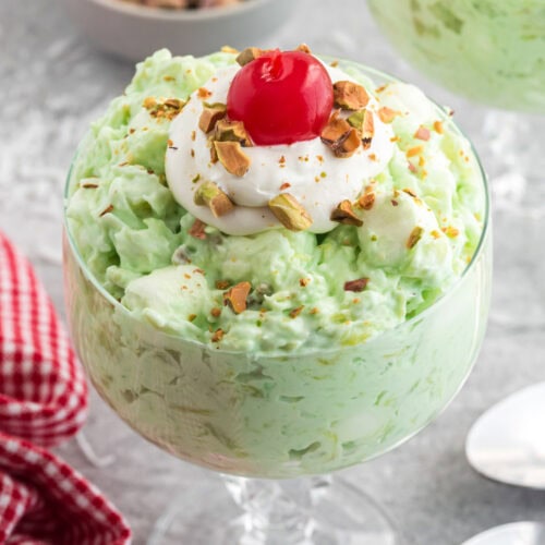 Close up photo of Watergate Salad in a bowl topped with cool whip and a cherry