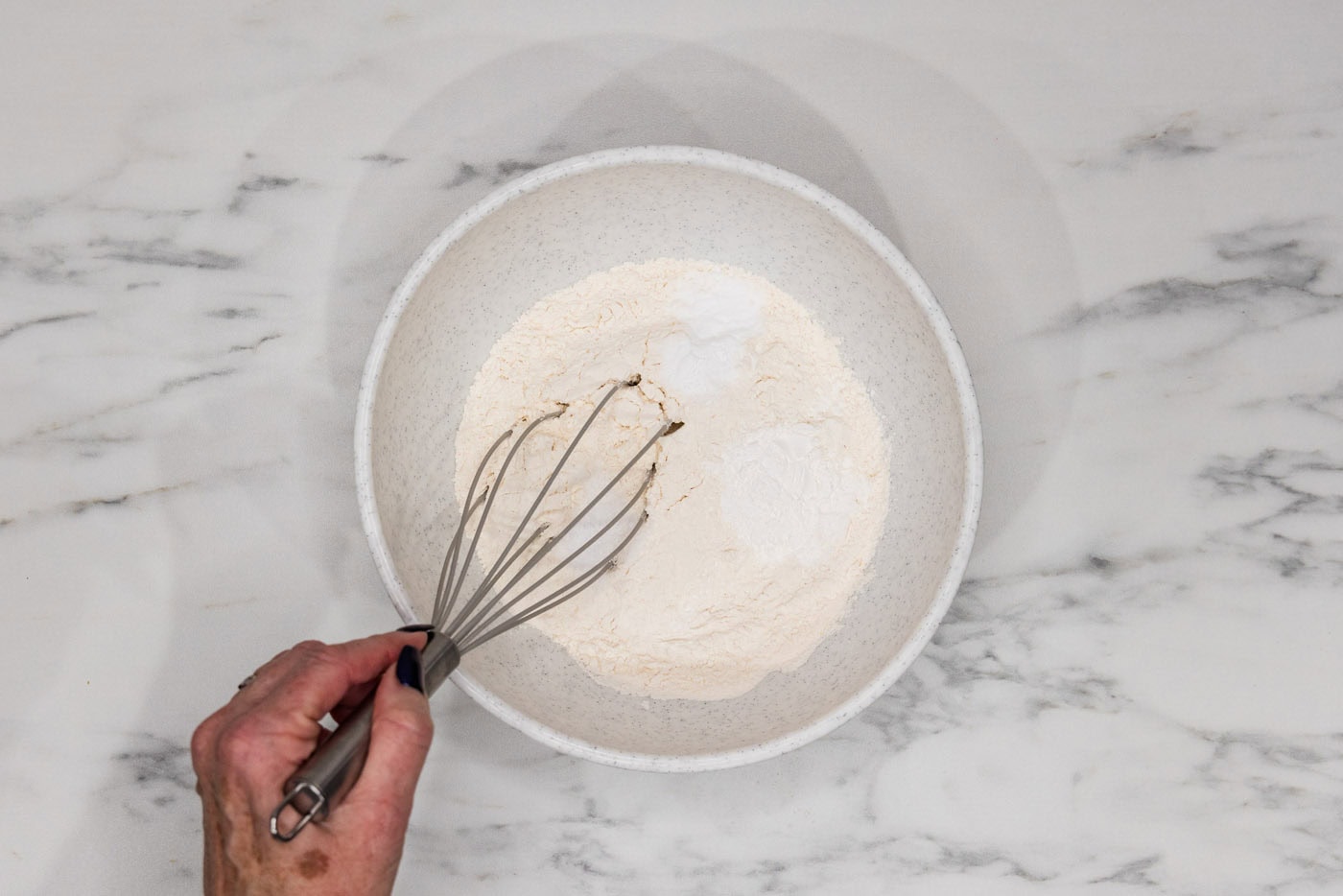 hand whisking flour, baking powder, baking soda, and salt in a bowl