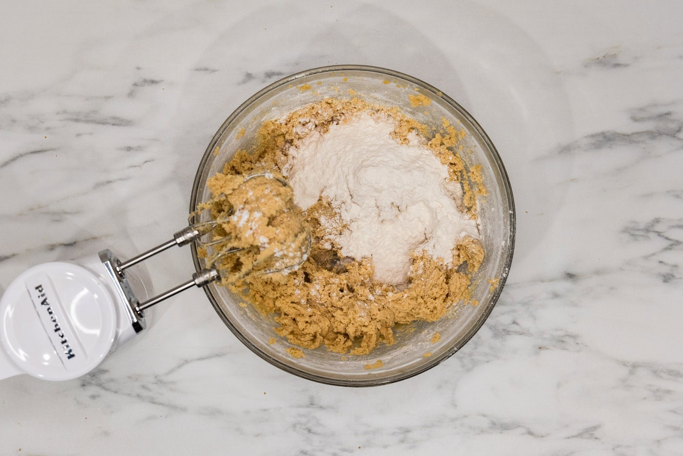 adding dry ingredients to wet cookie dough with a hand mixer