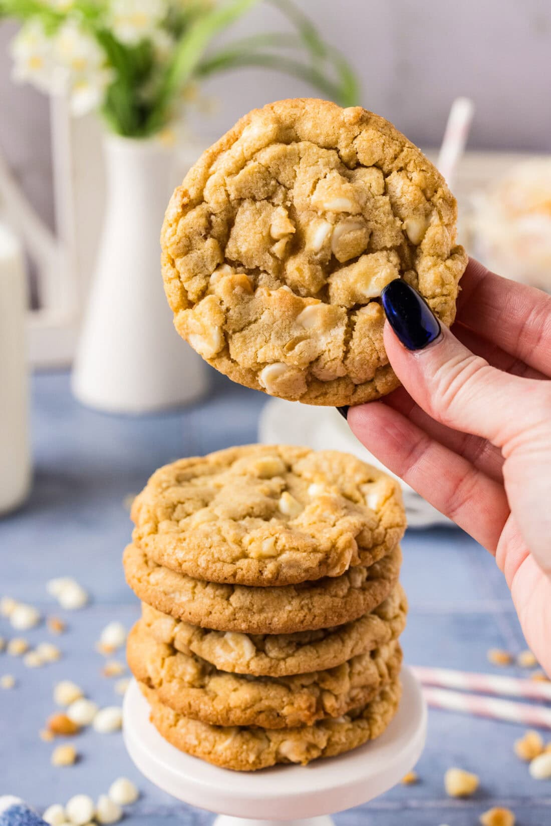 Hand holding up a White Chocolate Macadamia Nut Cookie above a stack of more cookies