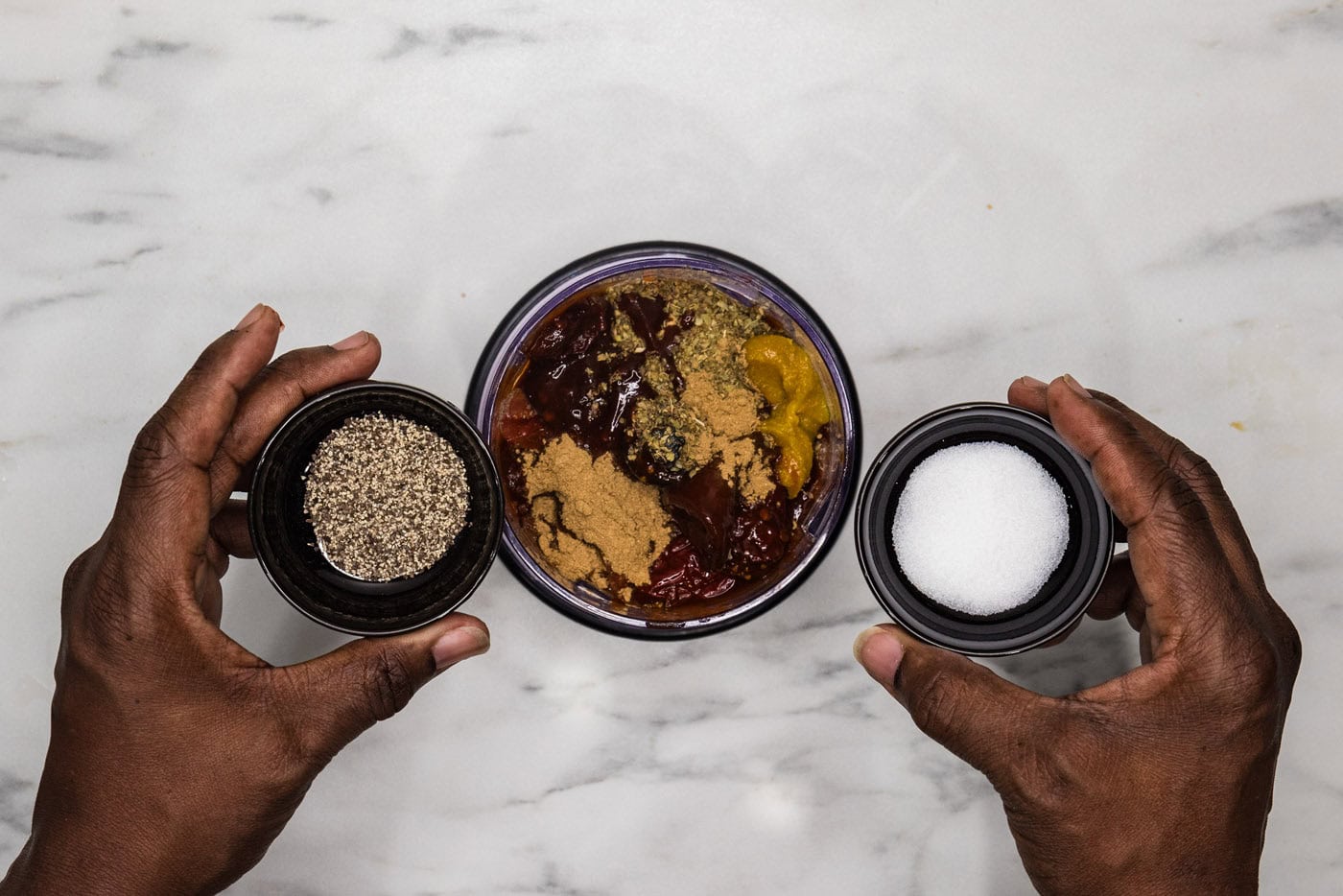 hand holding a bowl of salt and pepper over a food processor